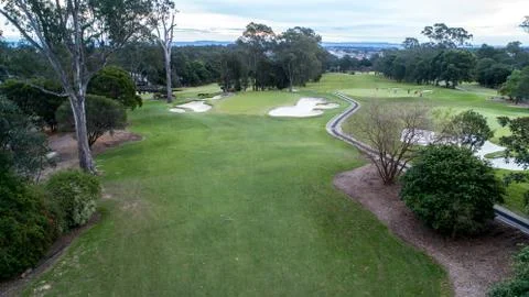 Golf Course tree lined fairway with green, flag, bunkers and golf cart pathways Stock Photos