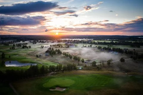 Golf course under warm sunset light with clouds and haze under field and tree Stock Photos