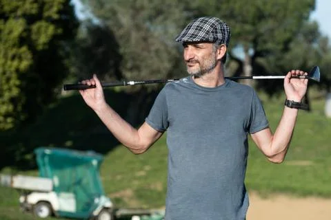 Golf player with a cap holding a golf club on his back Stock Photos