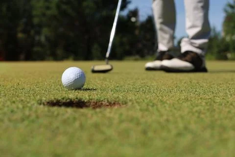 Golf player at the putting green hitting ball into a hole. Stock Photos