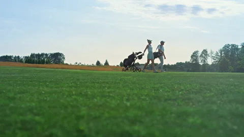 Golf players walk field on course. Golfing couple hold equipment clubs outside. Stock Footage 185531178