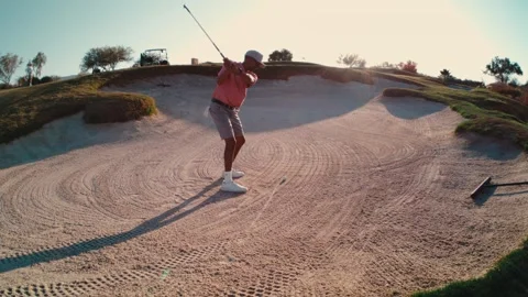 Golfer blasting out of a large sand bunker with an explosion of sand at golden Stock Footage 340991857