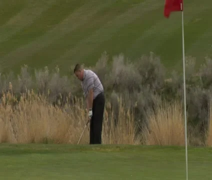 Golfer chips onto green with red flag and snowing mountains Stock Footage 21679554