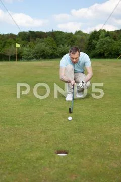 Golfer crouching while aiming at ball at golf course Stock Photos