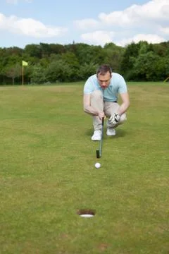Golfer crouching while aiming at ball at golf course Фото