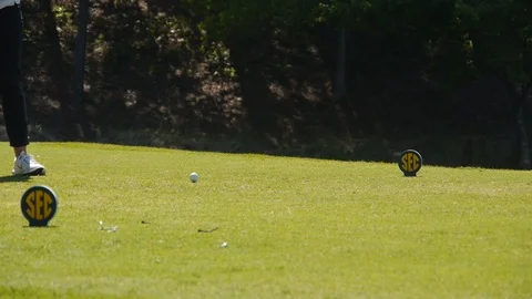 Golfer hits iron tee shot between SEC tee blocks at collegiate golf event Stock Footage 99984420