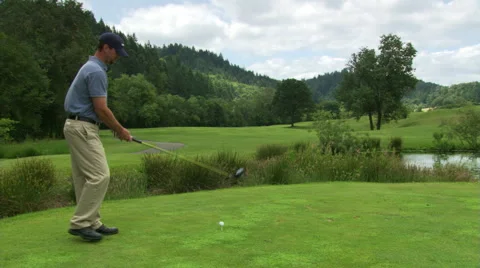 Golfer hitting ball over water hazard and down the fairway, tee remaining Stock Footage 59519009