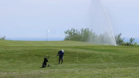 A golfer practices under the course's irrigation system Stock Footage 308644338