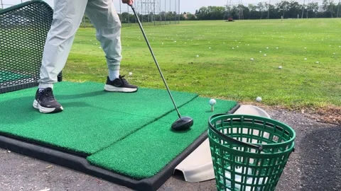 A golfer stands on a green driving range mat preparing to hit. Video stock 343673422