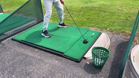 A golfer stands on a green driving range mat preparing to hit. 動画素材 343673653