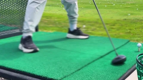A golfer stands on a green driving range mat preparing to hit a ball.  Video stock 344558492