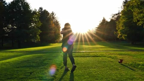 Golfer Teeing Off with Her Driver on Golf Course with Sunbeam and Lens Flare Видео 220477576