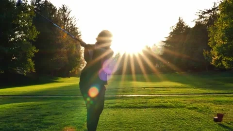 Golfer Teeing Off with Her Driver on Golf Course with Sunbeam and Lens Flare Stockbeeldmateriaal 220477577