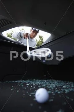 Golfer Using Golf Club To Retrieve Golf Ball Through Smashed Car Window