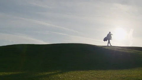 Golfer walking away from camera on green hilly slopes of golf course backlit Stock-Footage 336790466
