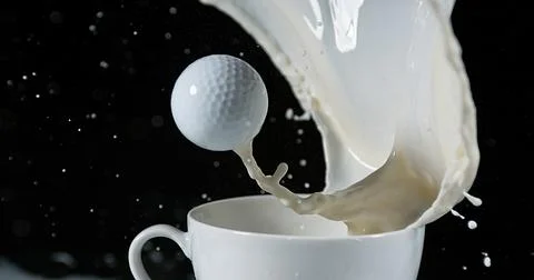 Golf's Ball in a Bowl with Exploding Milk against Black Background Stock Photos