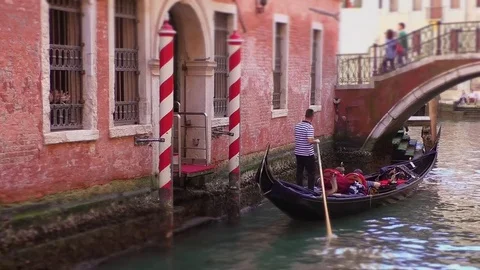 Gondolas in a canal in Venice Italy by evening - Tourists walk along the bridge Stock Footage