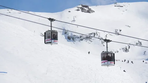 Gondolas at ski resort Les 2 Alpes drive above skiers crossing each other. Video stock 202320826