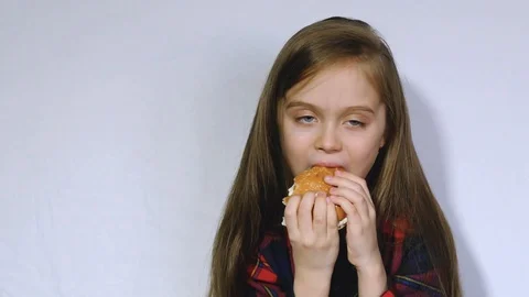 A good child eats a hamburger. A little girl in the kitchen is eating a Stock Footage 102393104