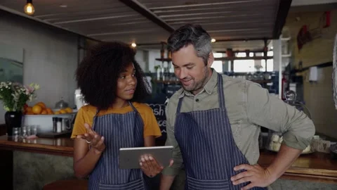 Good looking cafe owners, wearing aprons, discussing projects on tablet while Stock Footage 138592514