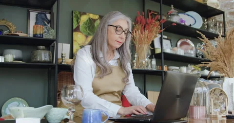 Good-looking careful calm grey haired mature woman in glasses working on laptop Stock Footage 143976306