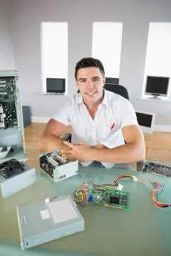 Good looking computer engineer sitting at desk smiling at camera Stock Photos