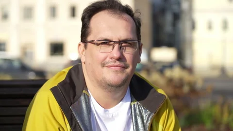 Good looking guy in glasses sitting on bench, relaxing in city park, looking Stock Footage 168566803
