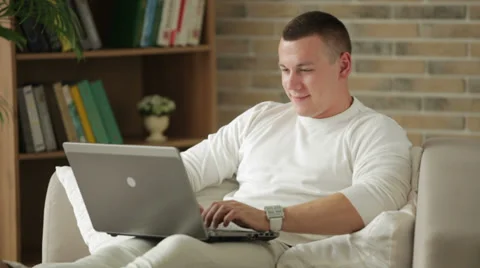 Good-looking guy sitting on sofa using laptop and smiling Stock Footage 28389653