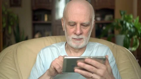 Good-looking handsome senior man sitting on chair at home. Using smartphone Stock Footage 74715662