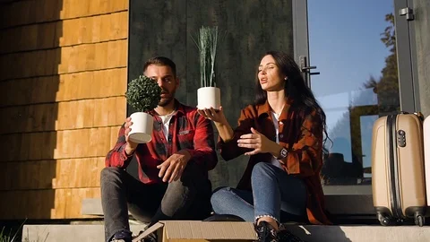 Good-looking happy 35s couple sitting on the house's steps and talking with one Stock Footage 121662390