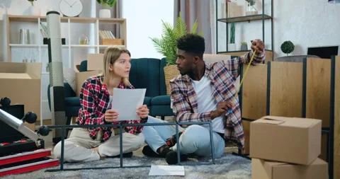 Good-looking happy smiling mixed race couple sitting on the carpet in their new Stock Footage 158564609