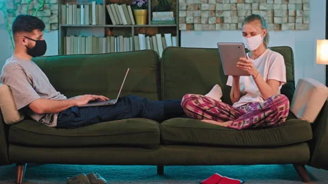 Good looking lady and guy with a protective mask on the sofa studying online Stock Footage 135601484