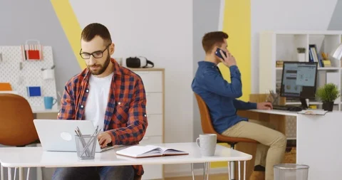 Good looking male worker in the glasses and plaid shirt working at the laptop Stock Footage 88464273