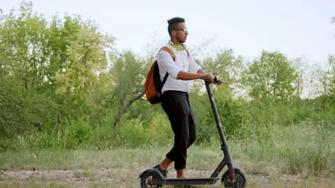 Good looking man Afro American walking down on the park with his electric Video stock 146978595