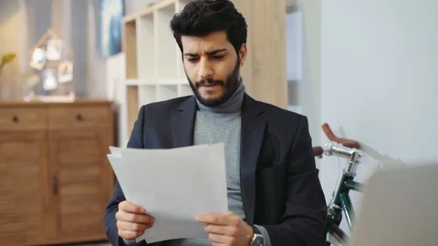 Good-looking man in a cozy office carefully reads the documents, finds what he Stock Footage 87392971