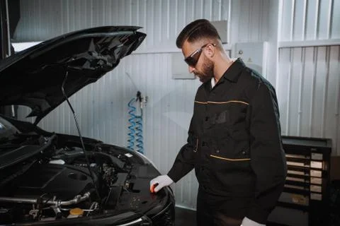 Good looking mechanic guy looking at the car engine in a car service Stock Photos