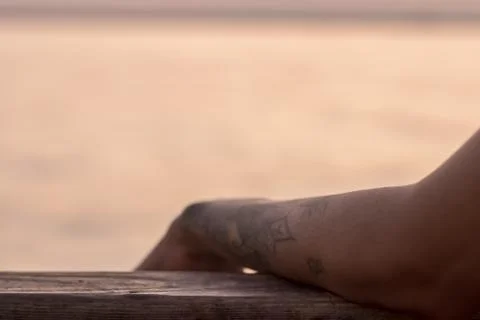 A good looking partial closeup shoot to tattooed girl arm - blurry sea as bac Stock Photos