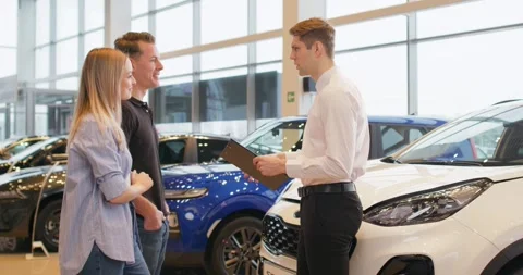 Good looking salesman showing some cars to a couple in a car dealership Vídeo Stock 259637905