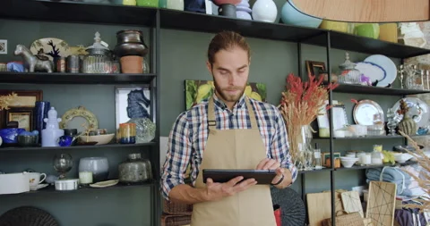 Good-looking satisfied smiling 30-aged bearded seller in apron uses tablet Stock Footage 143968885