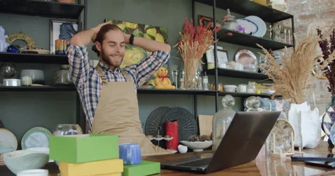 Good-looking satisfied smiling young bearded man in apron sitting in front of Stock Footage 143973177