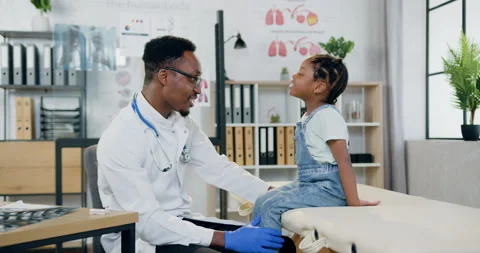 Good-looking smiling caring african american doctor talking with joyful little Stock Footage 156245408