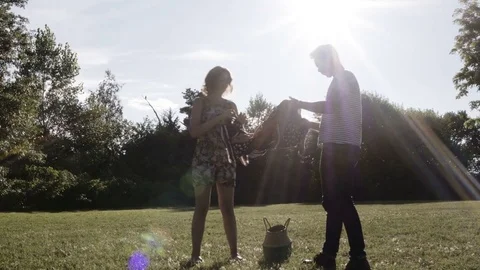 Good Looking Young Couple Laying Down A Picnic Blanket Backlit By The Sun. Stock Footage 80319725