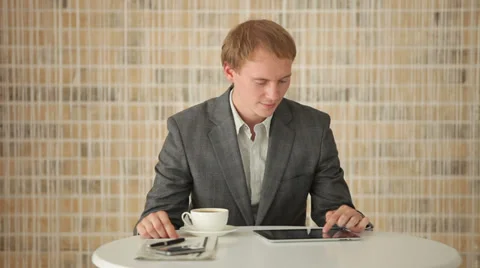 Good-looking young man sitting at table using touchpad and smiling at camera Stock Footage 34278249