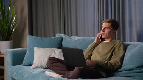 A good-looking young man works at a computer and talks on the phone from home Stock Footage 237511877