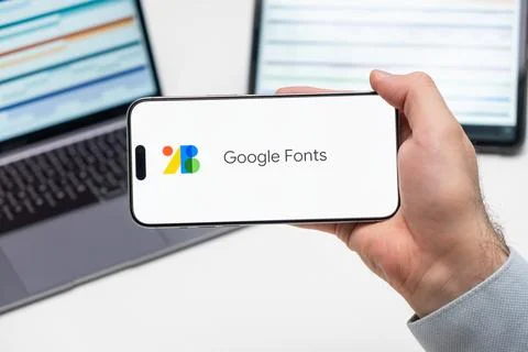 Google Fonts application logo on the screen of smart phone in mans hand, laptop Stock Photos