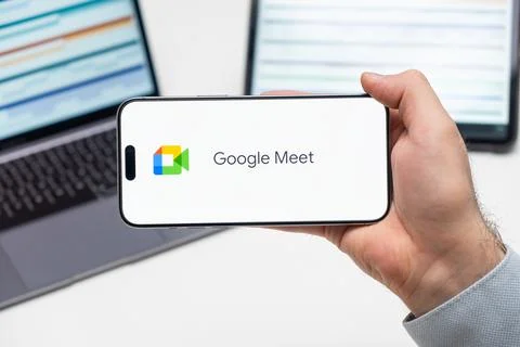 Google Meet logo of app on the screen of mobile phone held by man in front of Stock Photos