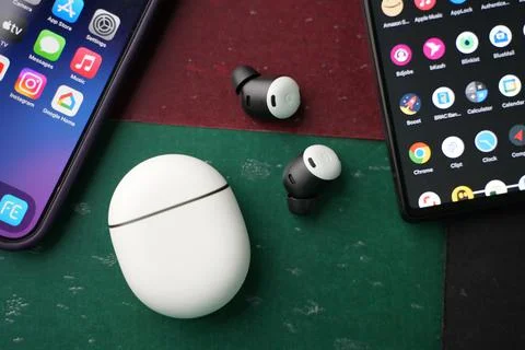 Google pixel ear buds on a black desk beside 2 smart phones Stock Photos