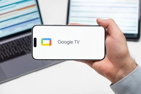 Google TV logo of app on the screen of mobile phone held by man in front of the Stock Photos