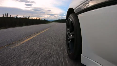 A GoPro camera mounted near the front wheel of a white sports car driving Stock Footage