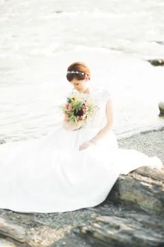 Gorgeous beautiful bride smiles while posing by the river with bouquet Stock Photos